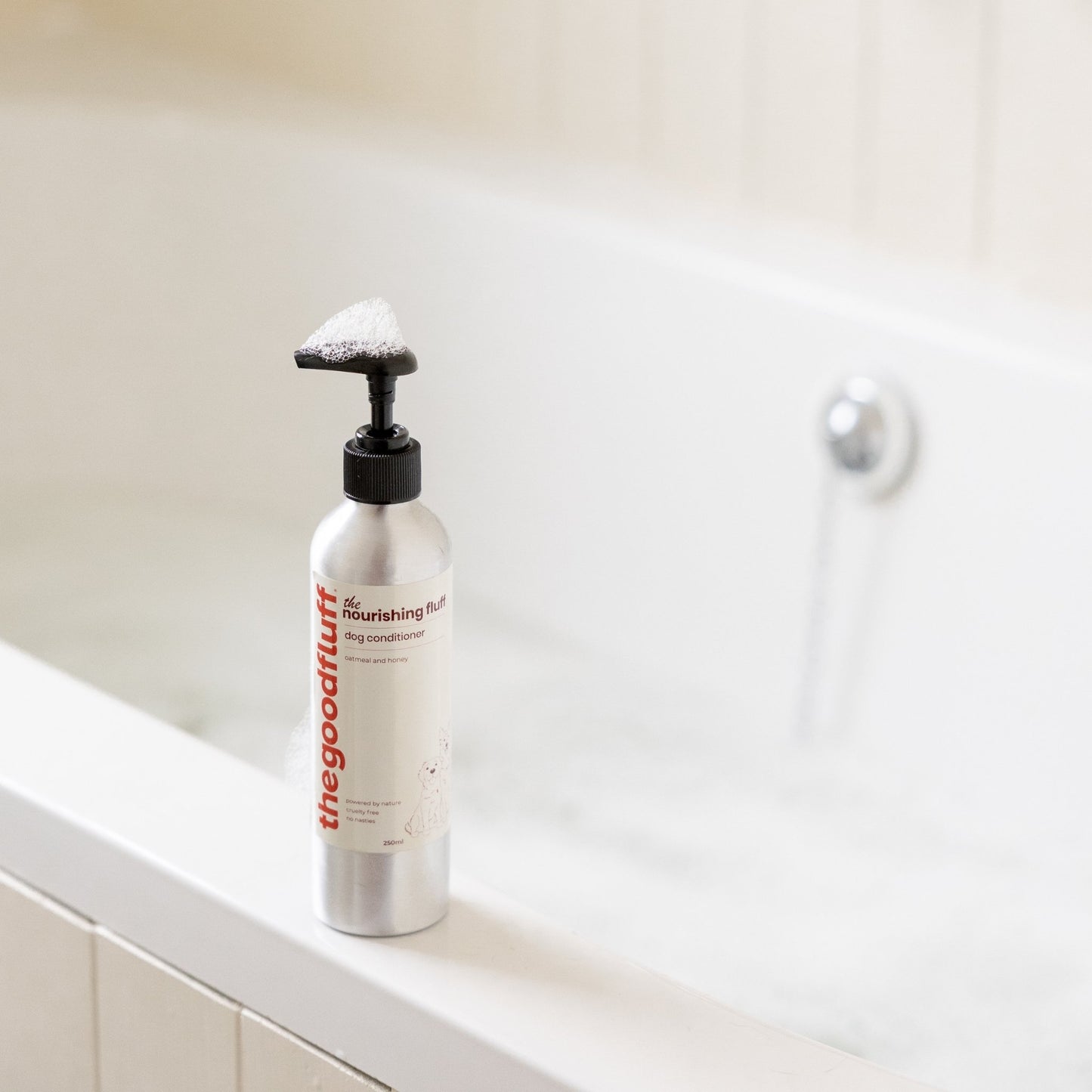 Bottle of the good fluff natural dog conditioner on the side of the bath with bubbles on the top